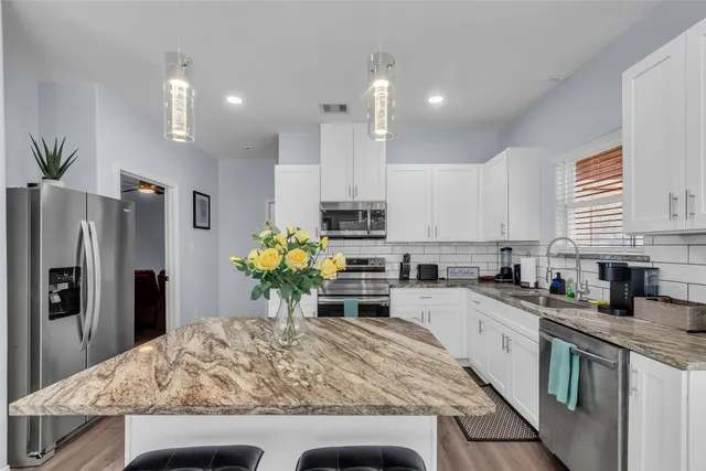 a kitchen with stainless steel appliances kitchen island granite countertop a refrigerator a stove a sink cabinets and a dining table