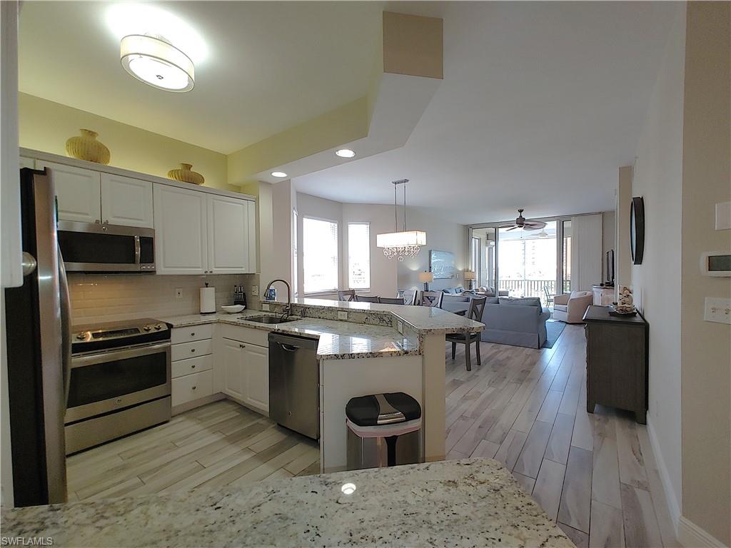 400 Flagship Drive, Unit 501 Naples, FL 34108 - Photo 9 of 38 a kitchen with stainless steel appliances granite countertop a stove top oven a sink dishwasher a dining table and chairs with wooden floors