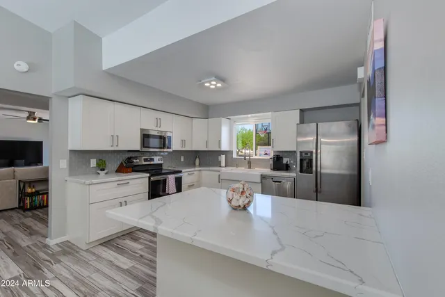 a kitchen view with stainless steel appliances kitchen island granite countertop a refrigerator a stove top oven a sink dishwasher and white cabinets with wooden floor