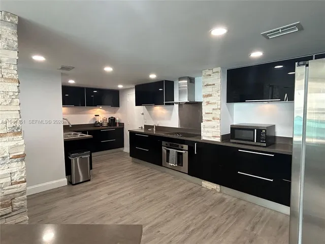 a kitchen with stainless steel appliances kitchen island granite countertop a refrigerator and a stove top oven with wooden floor