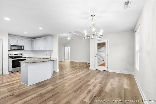 a large kitchen with granite countertop a stove top oven a sink dishwasher and white cabinets with wooden floor