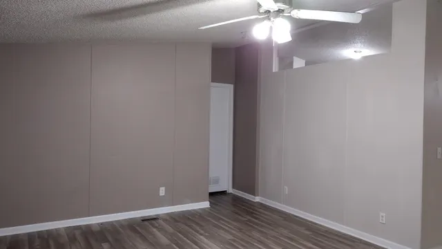 a view of an empty room with wooden floor and a chandelier fan