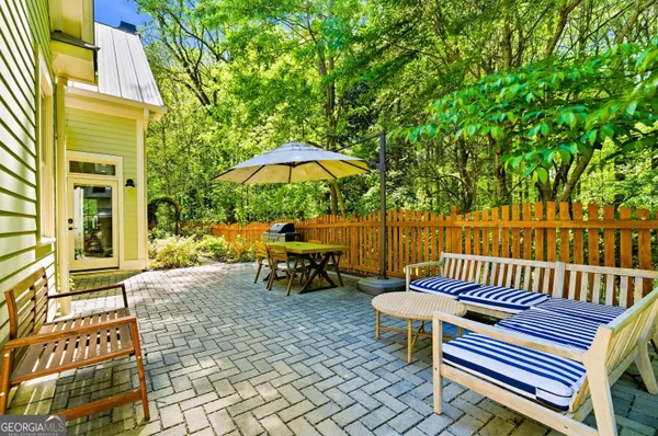 a view of a patio with a table and chairs under an umbrella with barbeque grill and wooden fence