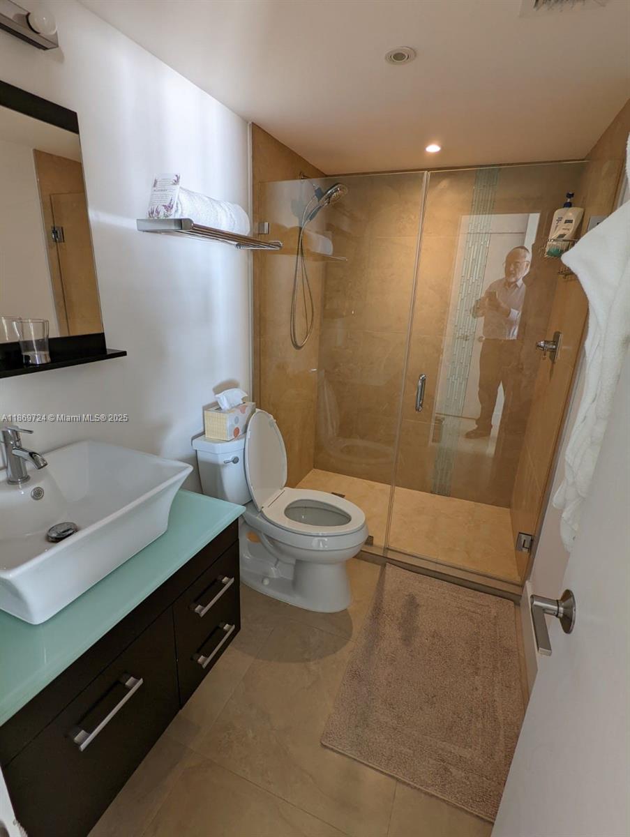 9273 Collins Avenue, Unit 1004 Surfside, FL 33154 - Photo 25 of 27 a bathroom with a sink a toilet a mirror and shower