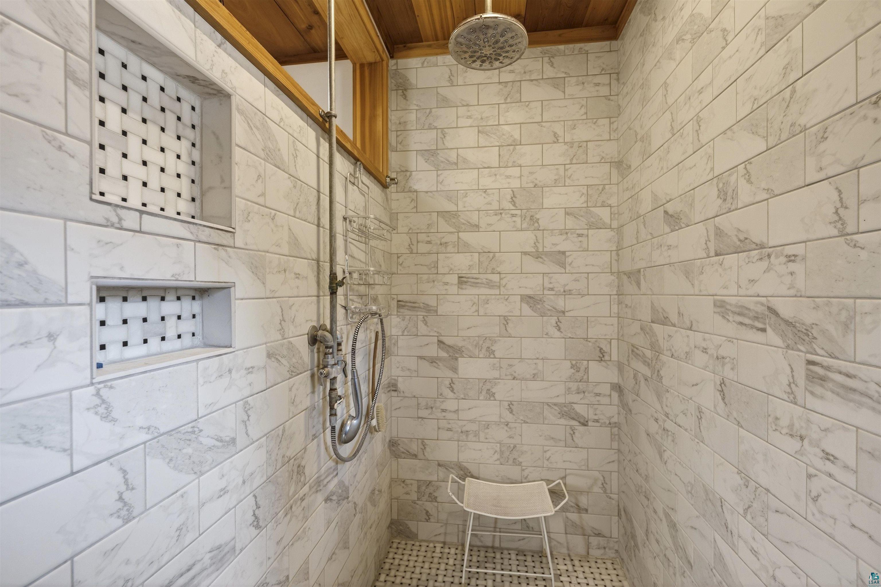 13885 Park Road Brule, WI 54820 - Photo 19 of 41 Shower featuring a rain shower head, hand-held shower, white subway tile walls with subtle gray veining, and two recessed niches with mosaic tile accents
