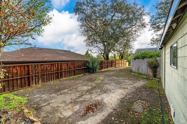 a backyard of a house with large trees and wooden fence