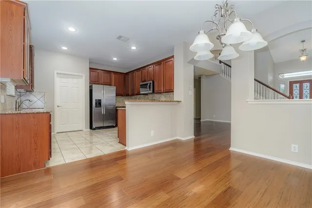 a view of a kitchen with a refrigerator a kitchen island wooden floor and a chandelier