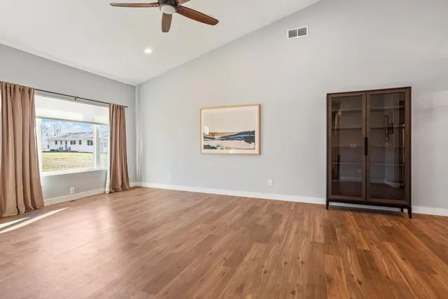 an empty room with wooden floor chandelier fan and windows