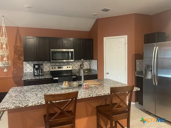 a kitchen with kitchen island granite countertop a stove refrigerator and microwave