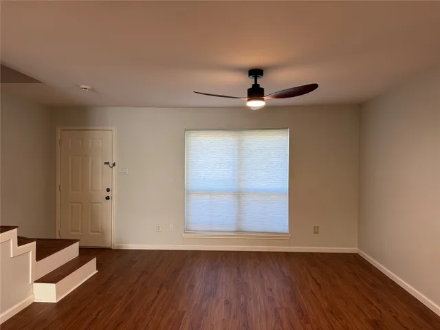an empty room with wooden floor ceiling fan and windows