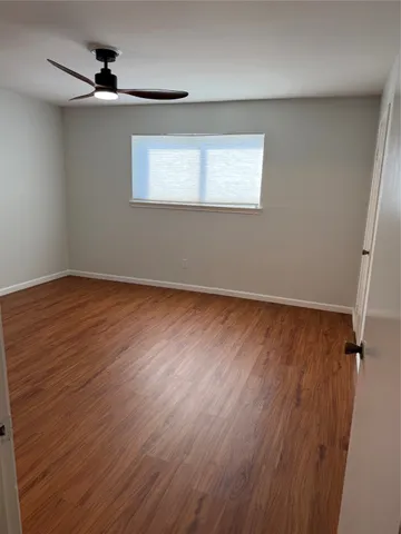 an empty room with wooden floor ceiling fan and windows