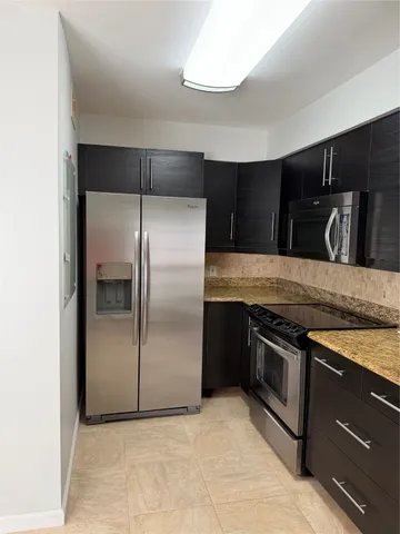 a kitchen with granite countertop a refrigerator and a stove top oven