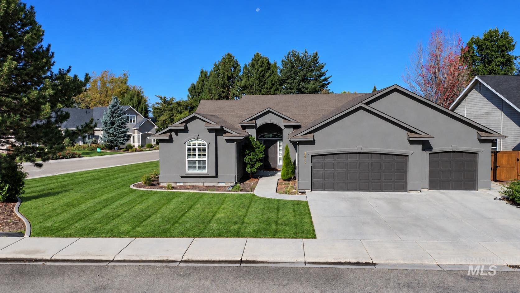 Stucco exterior with arched entry, two-car garage, concrete driveway, and manicured front lawn with mature trees