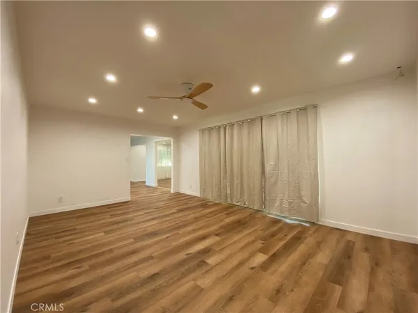 a view of an empty room with wooden floor and a kitchen