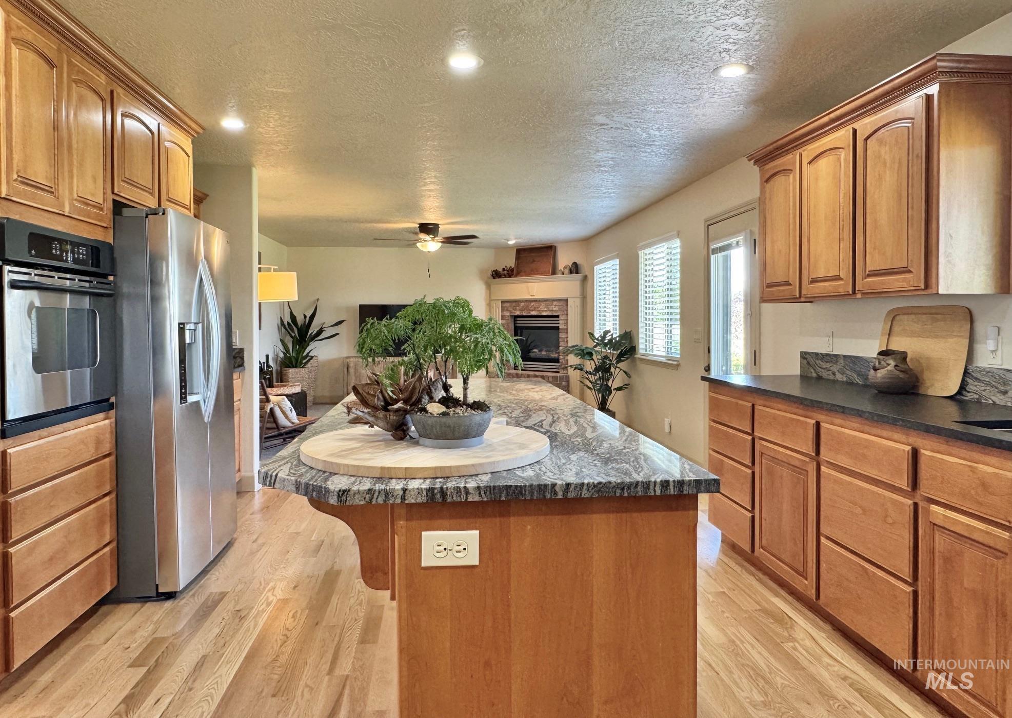 9299 Kemp Road Middleton, ID 83644 - Photo 8 of 50 Spacious kitchen featuring warm wood cabinetry, stainless steel appliances, a large center island with a stone-finish countertop, recessed lighting, and wood-finish flooring