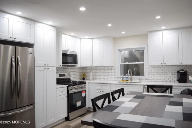 a kitchen with stainless steel appliances a refrigerator a stove a sink cabinets and a dining table with wooden floor