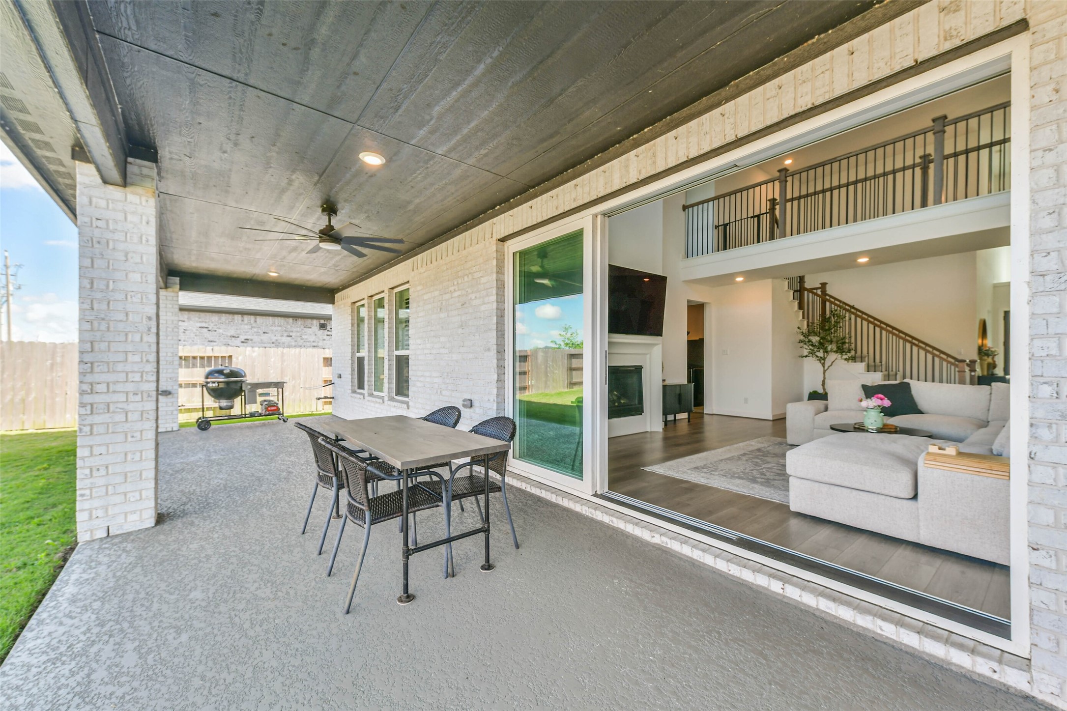 1612 Dayton Rdg Circle Friendswood, TX 77546 - Photo 44 of 50 spacious covered patio with ceiling fans and an outdoor dining area, ideal for entertaining. It overlooks a cozy living room with a fireplace and high ceilings, offering a seamless indoor-outdoor living experience.