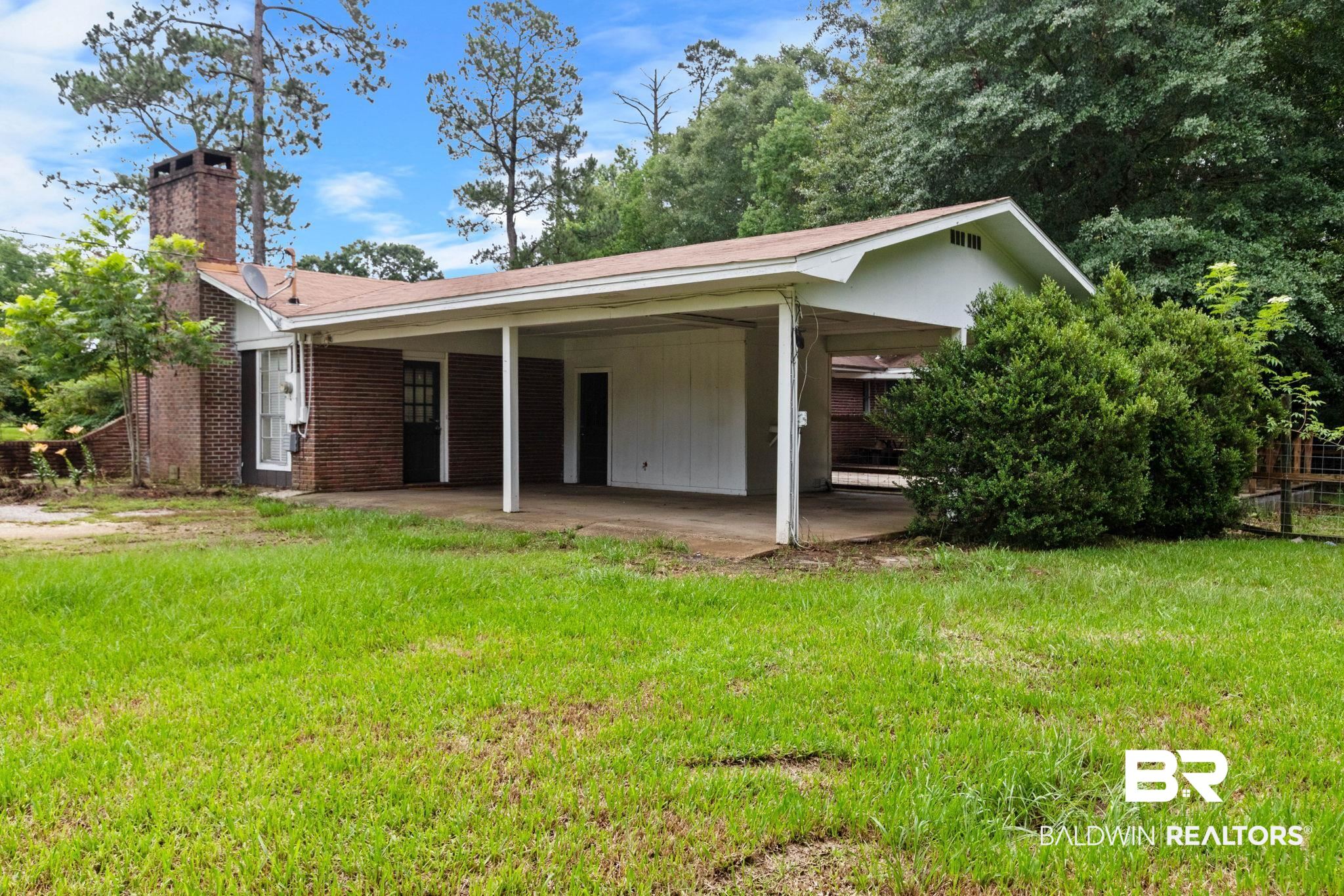 384 Old Bratt Road Atmore, AL 36502 - Photo 53 of 64 Brick exterior with an attached carport, featuring a prominent brick chimney and a surrounding grassy area