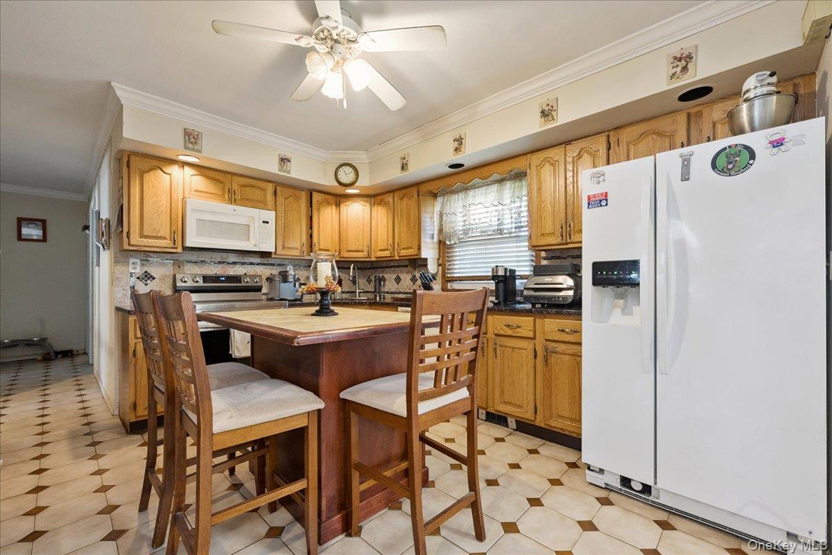 181 Springtime Lane North Levittown, NY 11756 - Photo 5 of 22 Kitchen with ornamental molding, white appliances, light flooring, backsplash, and a kitchen bar