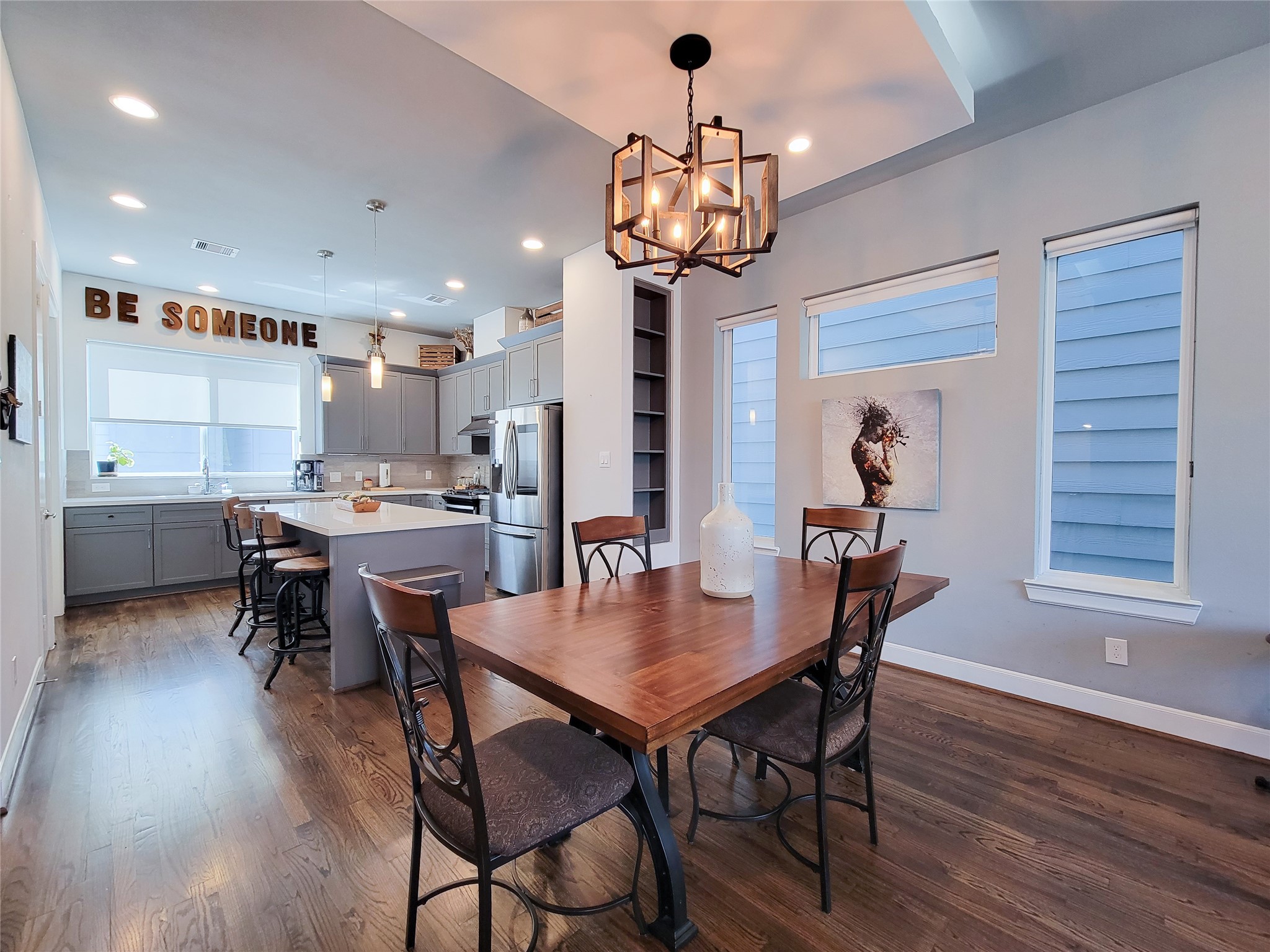 1705 Eado Point Lane Houston, TX 77003 - Photo 23 of 50 A modern kitchen and dining area with an open layout. It features hardwood floors, a spacious island with seating, stainless steel appliances, and plenty of natural light from multiple windows. The dining area includes a stylish light fixture and a wooden table with chairs, creating a cozy and inviting space.