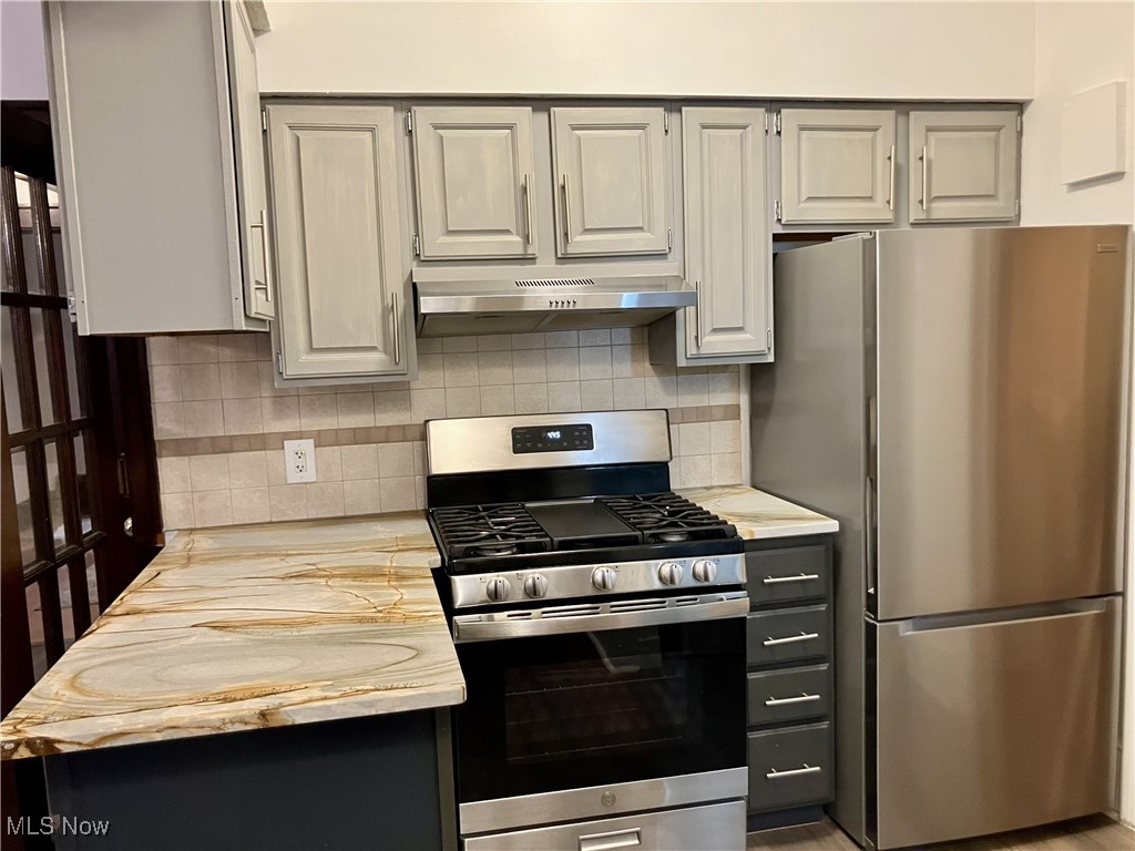 1006 Ridge Road Northwest Canton, OH 44703 - Photo 10 of 22 Kitchen with light countertops, appliances with stainless steel finishes, decorative backsplash, under cabinet range hood, and gray cabinetry
