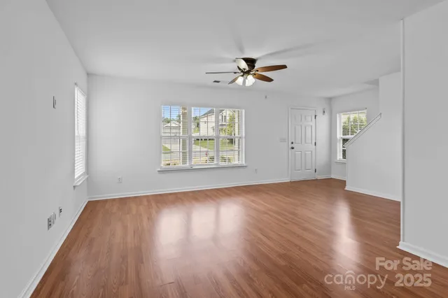 an empty room with wooden floor chandelier fan and windows