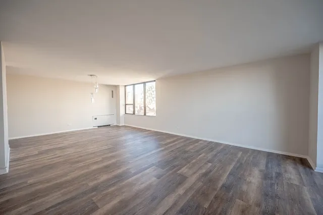 a view of an empty room with wooden floor and window