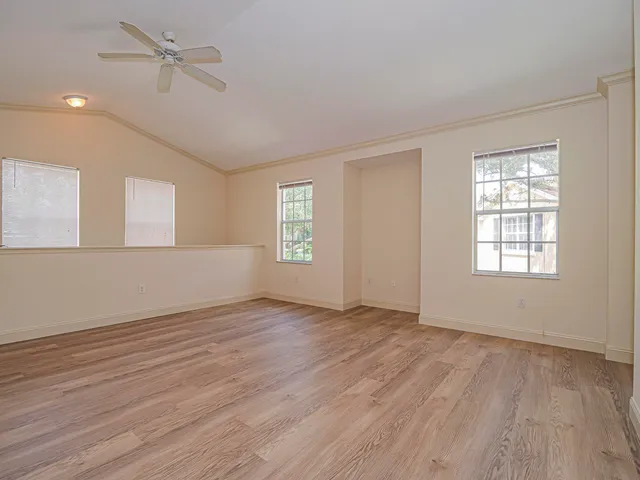 an empty room with wooden floor ceiling fan and windows