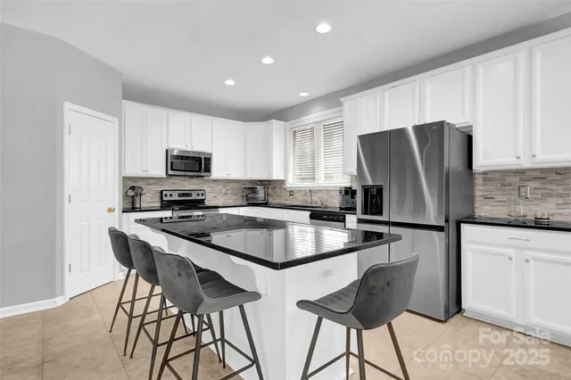 a kitchen with stainless steel appliances granite countertop a refrigerator a stove a sink a dining table and chairs