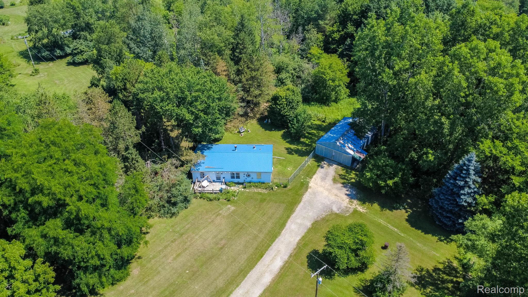 38 South Force Road Attica, MI 48412 - Photo 40 of 53 Rural property featuring a residence with a blue roof, a secondary outbuilding, extensive surrounding greenery, and a gravel driveway