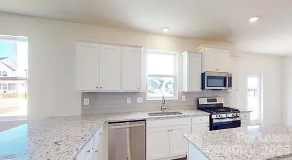 a kitchen with stainless steel appliances granite countertop a stove top oven a sink a refrigerator and white cabinets