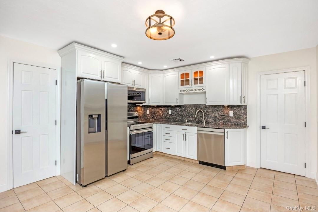 59 Nelson Road Selden, NY 11784 - Photo 14 of 38 Kitchen featuring glass insert cabinets, stainless steel appliances, white cabinets, dark stone counters, and recessed lighting