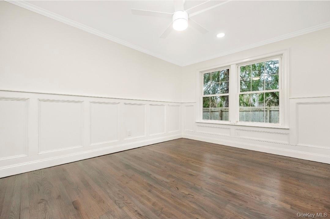 59 Nelson Road Selden, NY 11784 - Photo 23 of 38 Unfurnished room featuring dark wood-style floors, crown molding, a decorative wall, wainscoting, and a ceiling fan