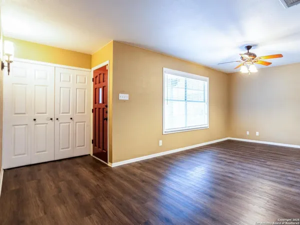 an empty room with wooden floor chandelier fan and windows