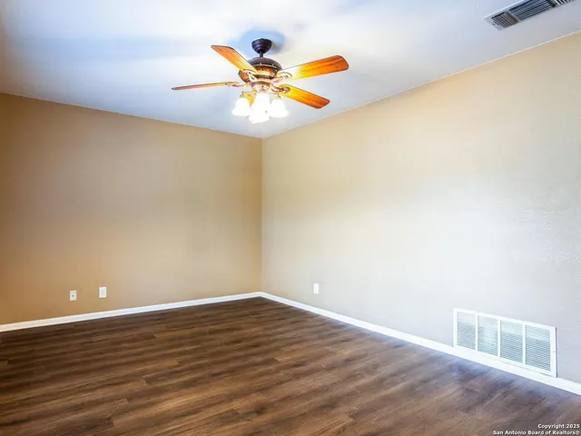 a view of an empty room with wooden floor and a ceiling fan