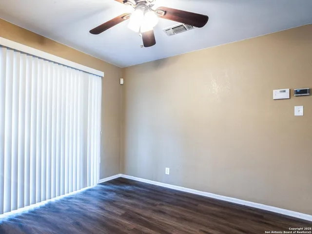an empty room with wooden floor chandelier fan and windows