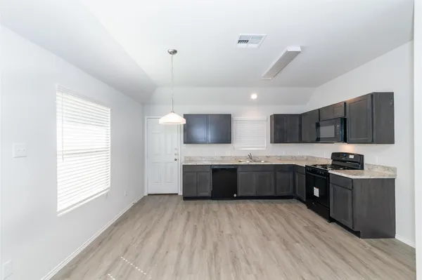 a large kitchen with stainless steel appliances kitchen island granite countertop a stove top oven a sink dishwasher a dining table and chairs with wooden floor