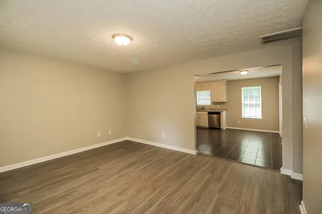 a view of empty room with wooden floor and kitchen view