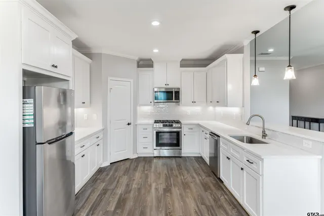 a kitchen with stainless steel appliances granite countertop a refrigerator a sink dishwasher a stove and white countertops with wooden floor