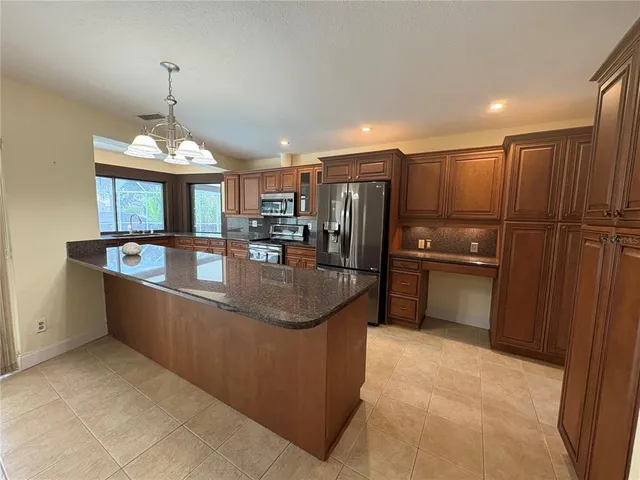a kitchen with stainless steel appliances granite countertop a refrigerator a sink a stove and a wooden cabinets