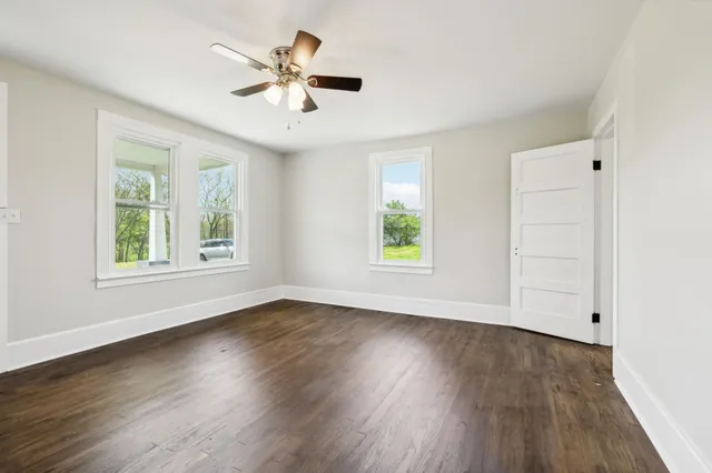 an empty room with wooden floor chandelier fan and windows