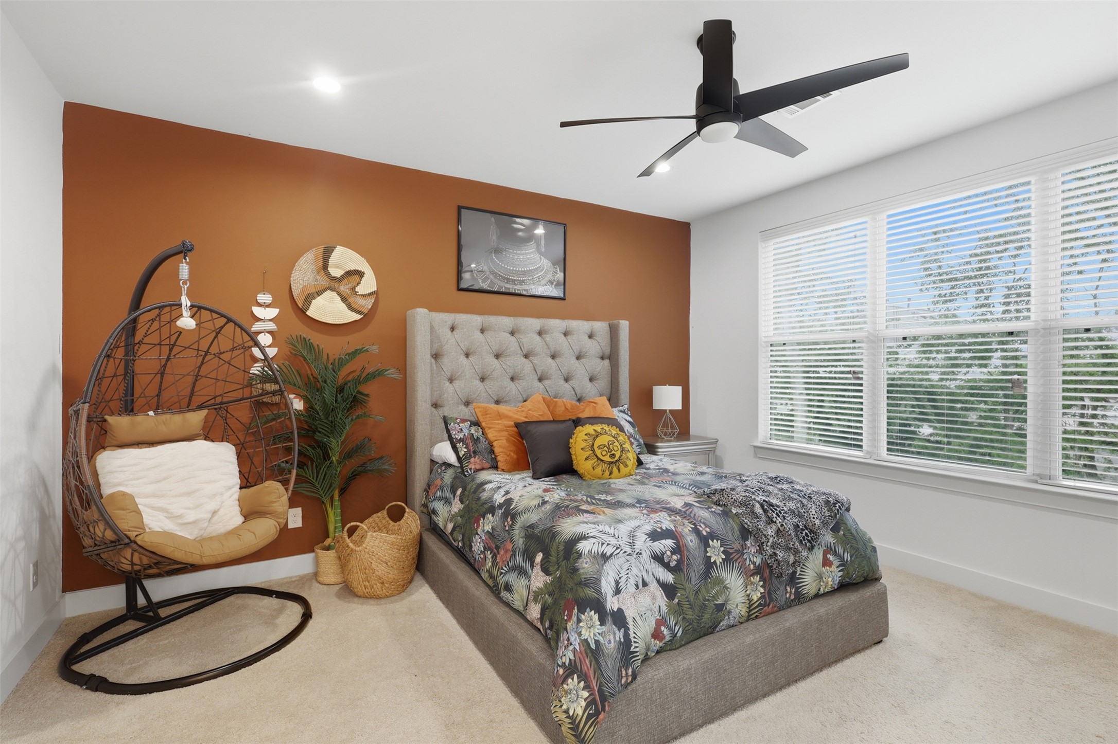 6833 Paris Street Houston, TX 77021 - Photo 18 of 23 This bedroom features a cozy and modern design with a textured gray bed, colorful bedding, and a stylish ceiling fan. A large window offers ample natural light, while a warm accent wall enhances the space. An inviting hanging chair and decorative elements complete the look.