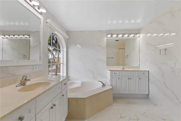 a bathroom with a granite countertop double vanity sink a mirror and a bathtub