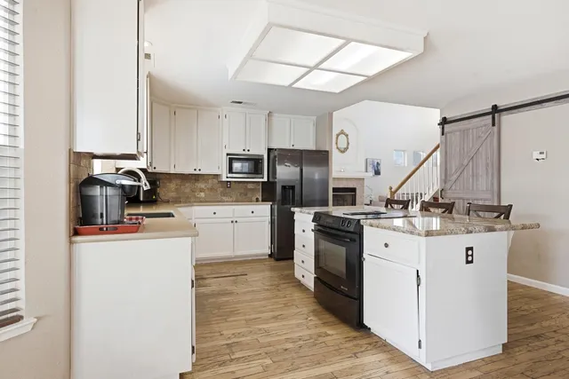 a kitchen with stainless steel appliances granite countertop a stove a refrigerator a sink a dining table and chairs