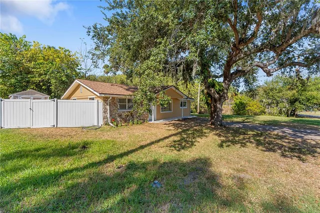 a backyard of a house with large trees and wooden fence