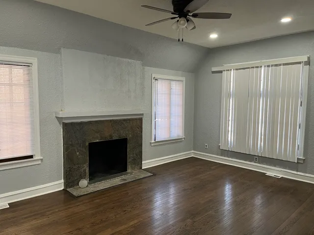 an empty room with wooden floor fireplace and windows