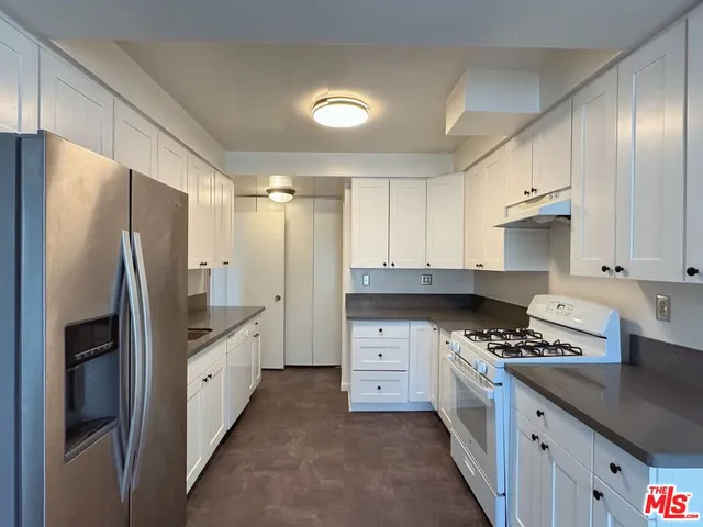 a kitchen with granite countertop a sink stove refrigerator and cabinets