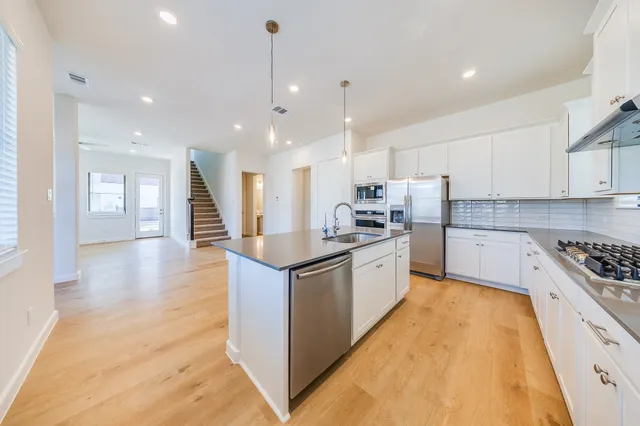a large kitchen with stainless steel appliances kitchen island granite countertop a stove a sink a refrigerator and white cabinets with wooden floor