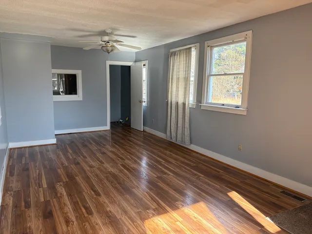 a view of an empty room with wooden floor and a window