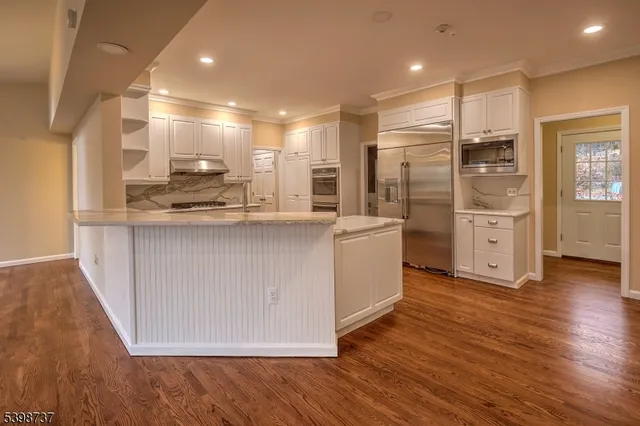 a kitchen with stainless steel appliances granite countertop a sink a stove a refrigerator and island with wooden floor
